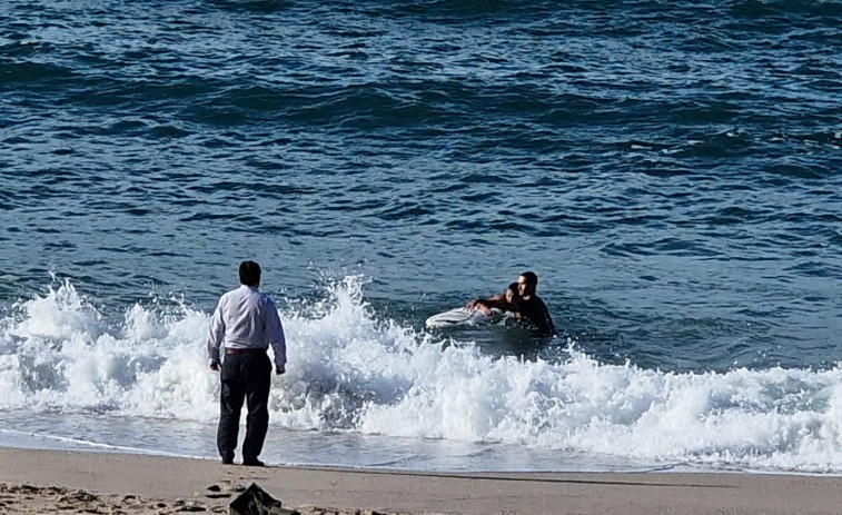 Un surfista y un viandante ayudan a una persona a salir del mar en el Orzán