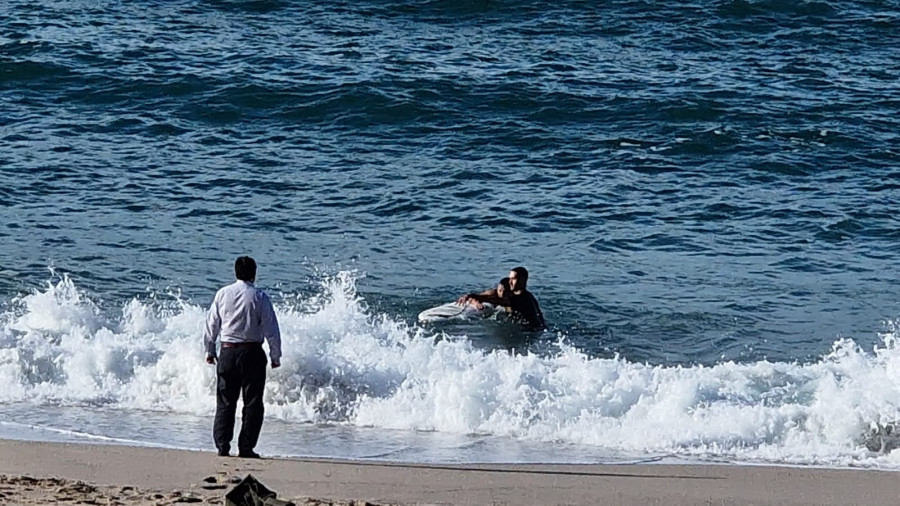 Un surfista y un viandante ayudan a una persona a salir del mar en el Orzán