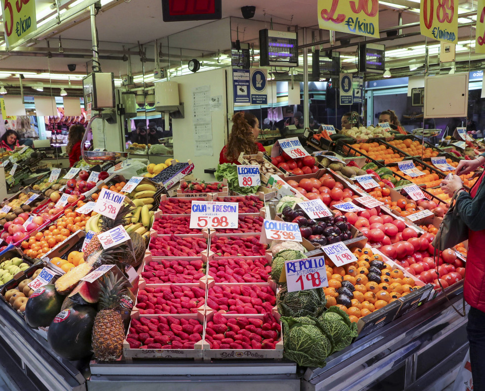 Una mujer espera ante un puesto de fruta del mercado