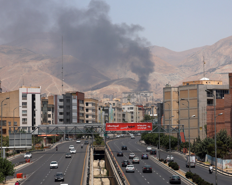 Varios coches salen de la ciudad mientras se eleva el humo provocado por el ataque a una refineria