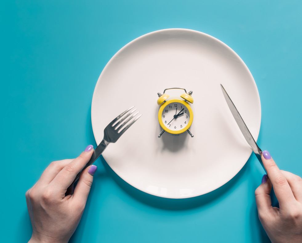 Manos sosteniendo un cuchillo y un tenedor sobre el despertador en un plato sobre fondo azul