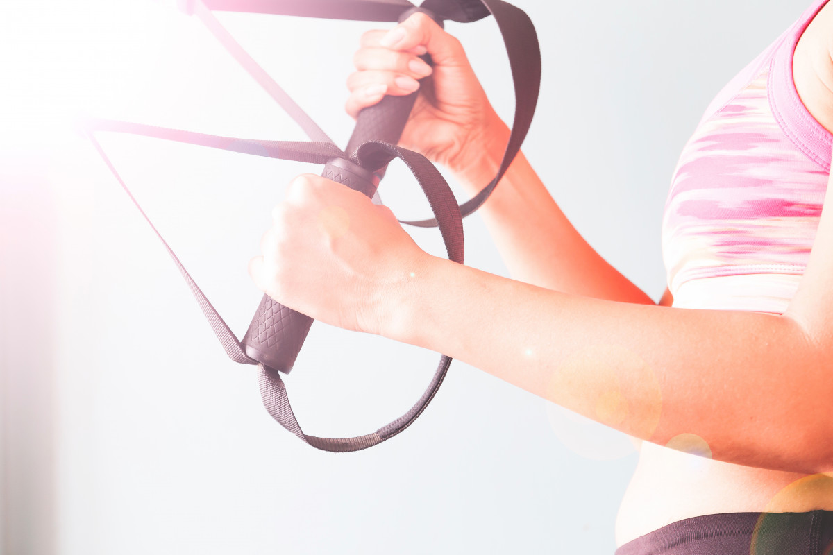 Fitness femenina en sujetador de deporte rosa con las manos en trx copiar el espacio